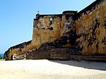 A fortified, but badly-faded yellow-coloured wall looks off into distant sea to the left.