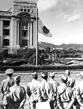 Homens em roupas militares observam o recolhimento de uma bandeira.