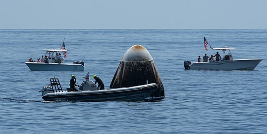 Private boats coming close to a crew working on the capsule.