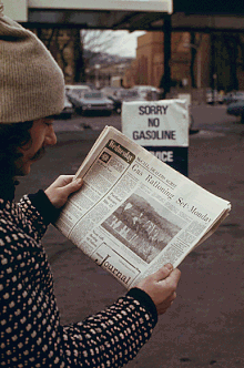 A man at a service station reads about the U.S. gasoline rationing system in an afternoon newspaper; a sign in the background states that no gasoline is available. 1974