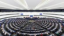 Rows and rows of people are assembled circularly in a huge chamber at the European Parliament