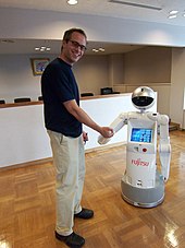 A man is shaking hands with a small humanoid robot