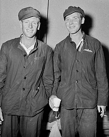 Two men in dark overalls and caps