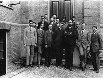 Fifteen men in suits, and one woman, pose for a group photograph