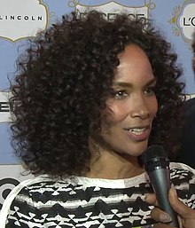 A woman with curly black hair is talking into a microphone.