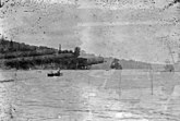 Photo of two men (centre left), in the distance, paddling a canoe across a lake.