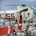 Photographie en couleur de l'équipage d'Apollo 7 descendant d'un hélicoptère pour arriver sur le pont du porte-avions Essex.