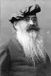 An elderly, bearded white man wearing glasses and a beret