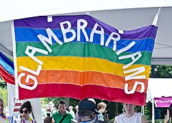 Ett antal personer står under en stor regnbågsfärgad flagga där det står GLAMBRARIANS.