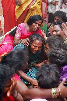 A group of seated transgender people and/or eunuchs dressed in saris mourn.