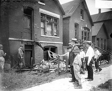 White men and boys standing in front of a vandalized house.