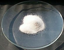 A clear glass dish on which is a small mound of a white crystalline powder.