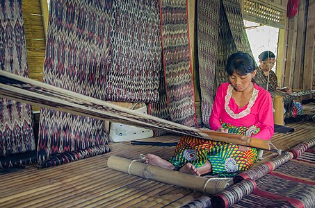 T'boli dream weavers using two-bar bamboo backstrap looms (legogong) to weave t'nalak cloth from abacá fiber. One bar is attached to the ceiling of the traditional T'boli longhouse, while the other is attached to the lower back. Philippines.[7][8]