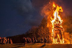 A burning bonfire of a towering 30 foot wickerman holding a sword. A crowd watches from below.
