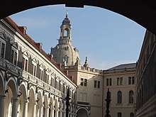 Barevná fotografie s průhledem kamenným obloukem na nádvoří rezidenčního zámku směrem ke kupoli kostela Frauenkirche