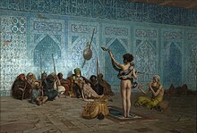 This painting shows the back side of a naked man standing with a snake wrapped around his waist and shoulders. The man is lifting up the head of the snake with his left hand. Another man to his right is sitting on the ground playing a pipe. A group of 10 men are sitting on the floor facing the snake handler with their backs against an ornate blue mosaic wall decorated with Arabic calligraphy.