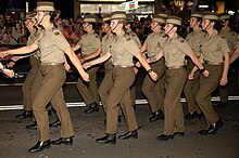 Colour photo of men and women marching down a street while wearing green military uniforms