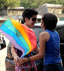 Two women smile at each other and hold hands while one of the women holds a LGBT rainbow flag