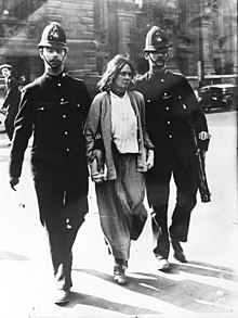 Une femme en état d'arrestation marche entre deux policiers.