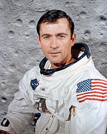 Portrait photograph of Young in an Apollo spacesuit in front of a lunar surface background