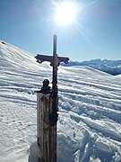 Photographie d'une croix noire dans la neige en hiver 2022, au milieu des montagnes, en bois et en métal.