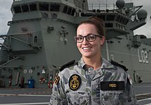 A woman wearing a camouflaged military uniform on the deck of a ship