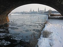 Barevná fotografie s průhledem pod klenbou mostu na zasněžený břeh a částečně zamrzlou hladinu Labe