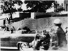 John F. Kennedy is fatally shot in the head, with Jacqueline Kennedy sitting beside him. Jacqueline can be seen turning over and looking at him at that moment.