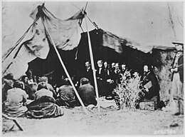 A black-and-white photo of a group of people sitting under a tent