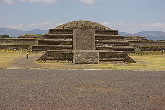 Adosada platform in the midground, Pyramid of the Feathered Serpent behind the platform, person beside a small platform in the foreground gives scale