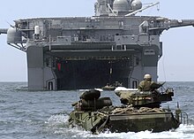 foto colorida de AAVs nadando se aproximando do convés de um navio de assalto anfíbio