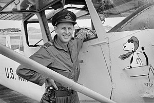 Smiling man in overalls with peaked cap next to aircraft featuring image of Snoopy as the Red Baron