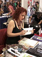 A red-hair woman wearing a black shirt and signing a book, with several other people behind her.