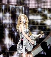 Swift singing on an acoustic guitar wearing a sparkly dress