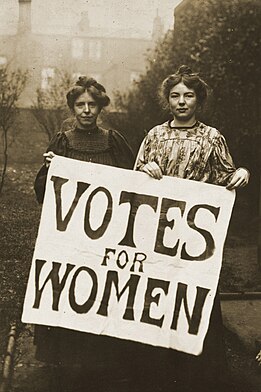 Duas mulheres segurando uma placa em que está escrito, em inglês, "Votos para Mulheres"