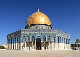 An octagonal, multi-colored building, the upper trim of which is inscribed in Arabic, topped by a golden-plated dome