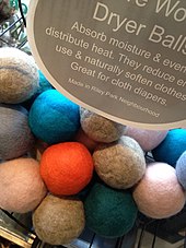 A large pile of multicolored felted wool balls sit in a basket below a sign labeling what they are and their uses.