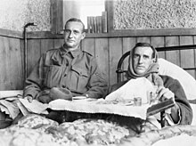 Hugo Thrussel, lying in bed with scarf wrapped around his head, sitting to the side of the bed is his brother Ric Thurssel, in a military uniform with seargent's stripes on his upper sleeve