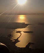 The San Francisco–Oakland Bay Bridge, Yerba Buena Island, Treasure Island, and San Francisco, in an afternoon aerial view looking into the sun
