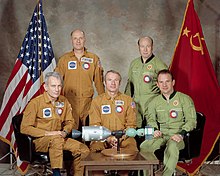 The five crew members of Apollo–Soyuz Test Project sit around a miniature model of their spacecraft.