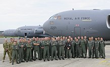 A group of people wearing overalls standing together in front of three grey aircraft are visible in the background.