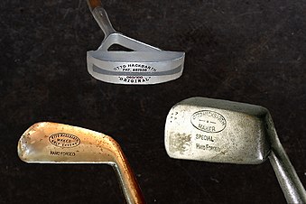 3 of Otto Hackbarth's original golf club designs. The famous Hackbarth putter is pictured in the top center. The clubs are on a dark background.