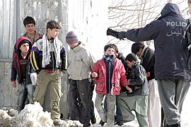 A member of the Afghan National Police trying to control local children awaiting the distribution of goods from the U.S. military for the winter months.