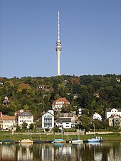 Barevná fotografie s pohledem na štíhlou televizní věž nad krajinou předměstí