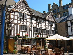 A timber-framed building, three floors high with a gabled roof. There are tables and chairs outside.