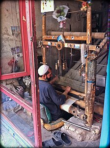 Weaving at a pit loom; the frame is built shorter, but set over a pit, so that the treadles are below ground level. Herat, Afghanistan.