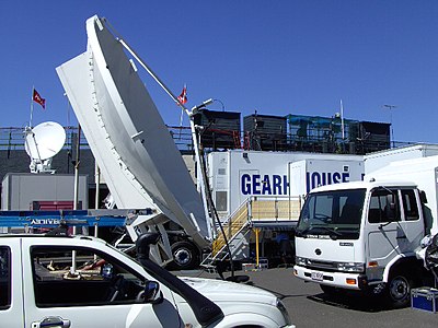 OB for tennis tournament: Extendible-sided production van, satellite dishes, generator truck; see two OB cameras and three announcing booths at top of stadium beyond. Kooyong, Victoria, Australia, 2008