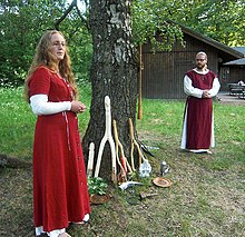 A man and a woman standing outdoors by a tree, wearing red and white robes