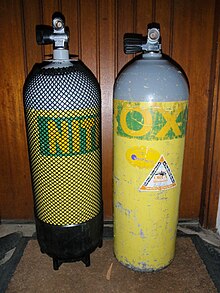 Two cylinders stand next to each other. On the left is a round-bottomed 15-litre steel cylinder with a plastic boot, and on the right a flat-bottomed 12.2-litre aluminium cylinder without boot. Both cylinders are the same outside diameter (203 mm), but the smaller-volume aluminium cylinder is slightly higher than the larger-volume steel cylinder, even though the steel cylinder is standing on a boot and has a rounded bottom.