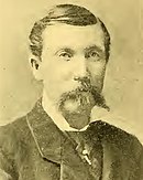 Sepia toned photo of a man with a moustache in civilian dress.